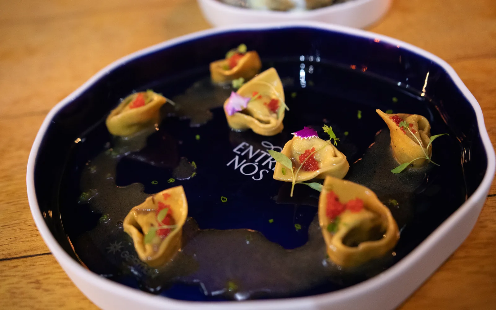 Tortelli servidos em caldo no prato assinado Entre Nós